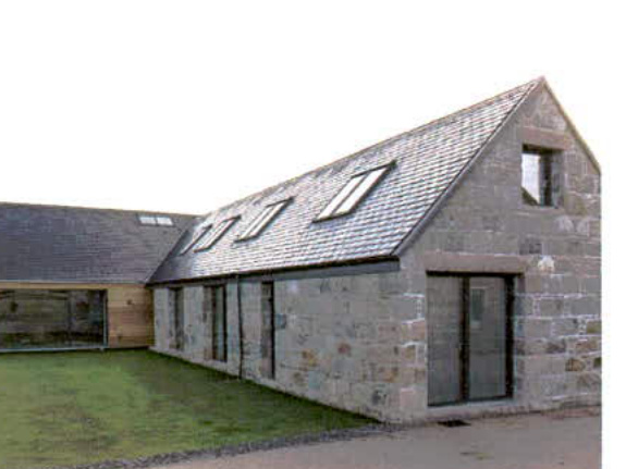 A photograph showing a stone building with a pitched slate roof and skylights, appearing to be a barn conversion or new rural dwelling.