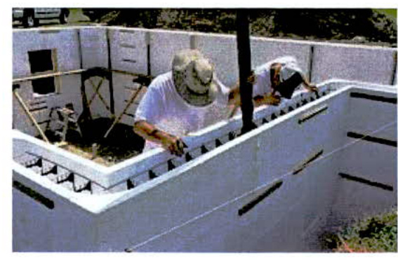 A photograph showing construction workers building white block walls, likely the foundation or lower level of a new dwelling.