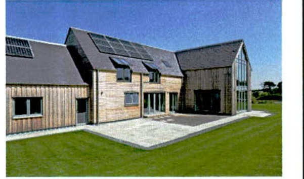 A photorealistic rendering of a large, modern timber-clad building complex featuring solar panels on the roof, a paved driveway, and a green lawn.