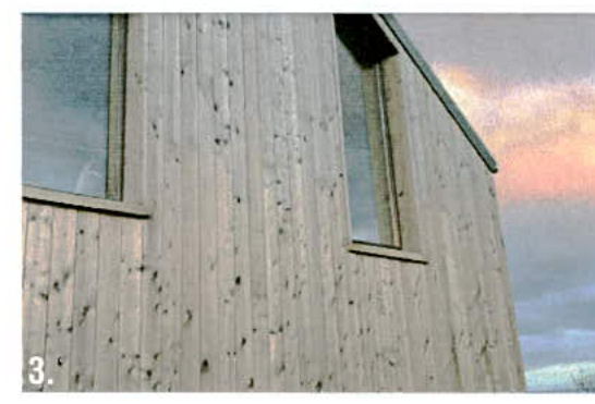 A close-up photograph of a building's exterior corner featuring vertical wooden cladding and two windows against a cloudy sky.