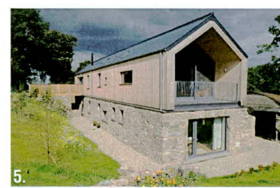 A photograph of a modern two-storey dwelling featuring a stone ground floor and timber upper cladding with a balcony, set in a grassy rural environment.
