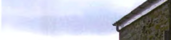 A close-up photograph showing the corner of a stone building with a gutter and roofline against a cloudy sky.