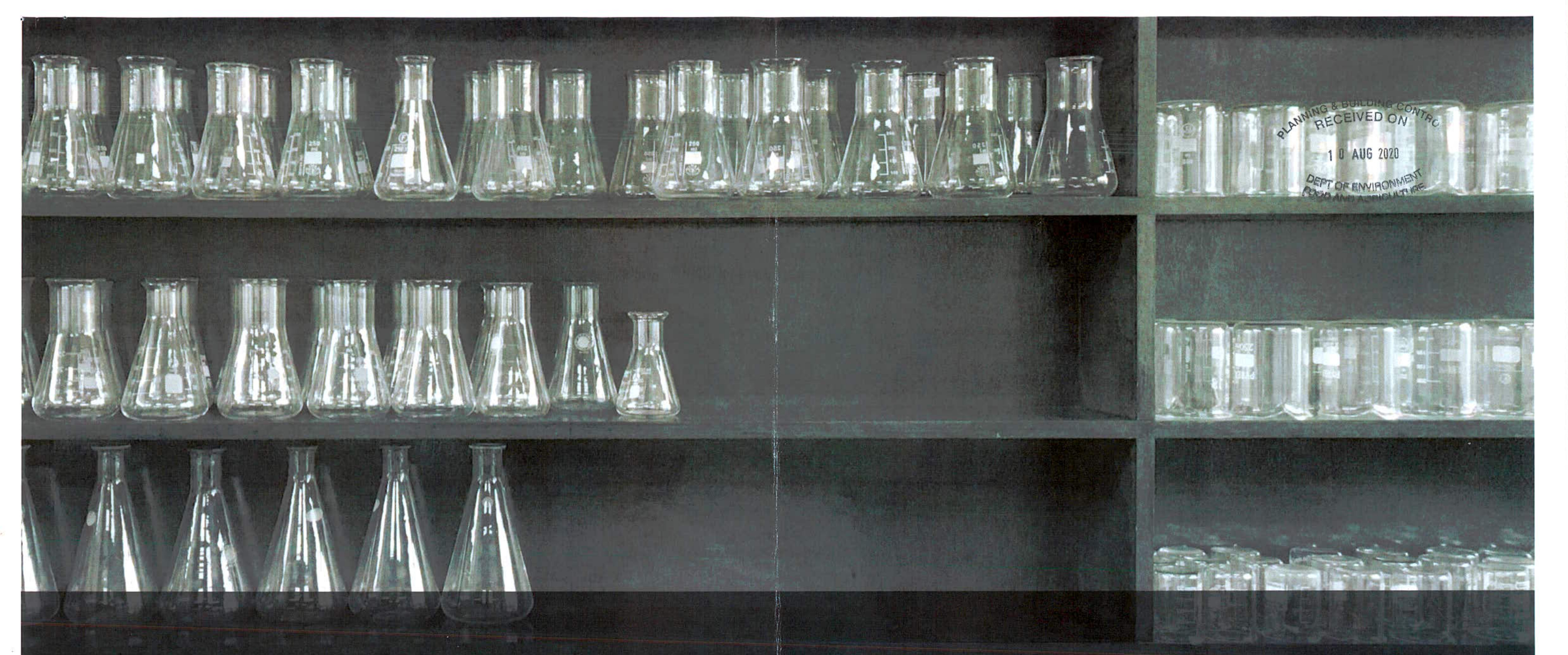 A photograph showing shelves filled with laboratory glassware, including conical flasks, with a planning department received stamp visible on the right.