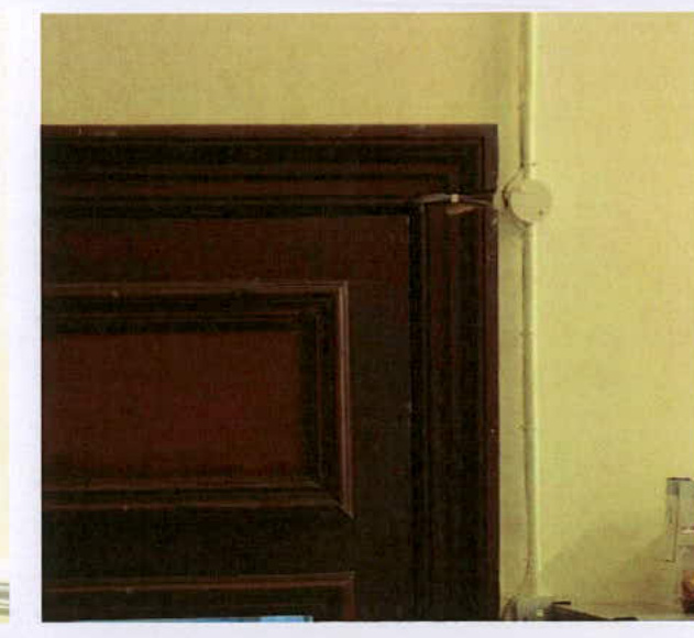 A close-up photograph showing a dark wooden internal door frame and a white vertical pipe running along the adjacent wall.