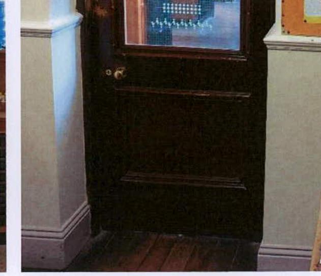 A close-up photograph of a dark wooden door with a glazed upper panel and brass handle, situated between white skirting boards.