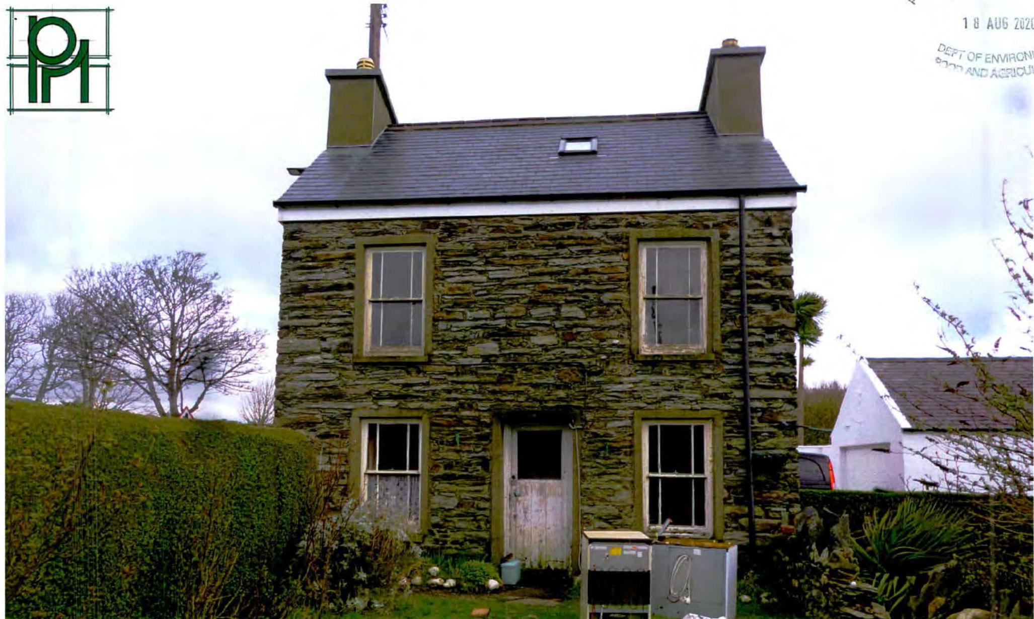 A photograph of a two-story stone house with a slate roof and sash windows, featuring a hedge and utility boxes in the foreground.