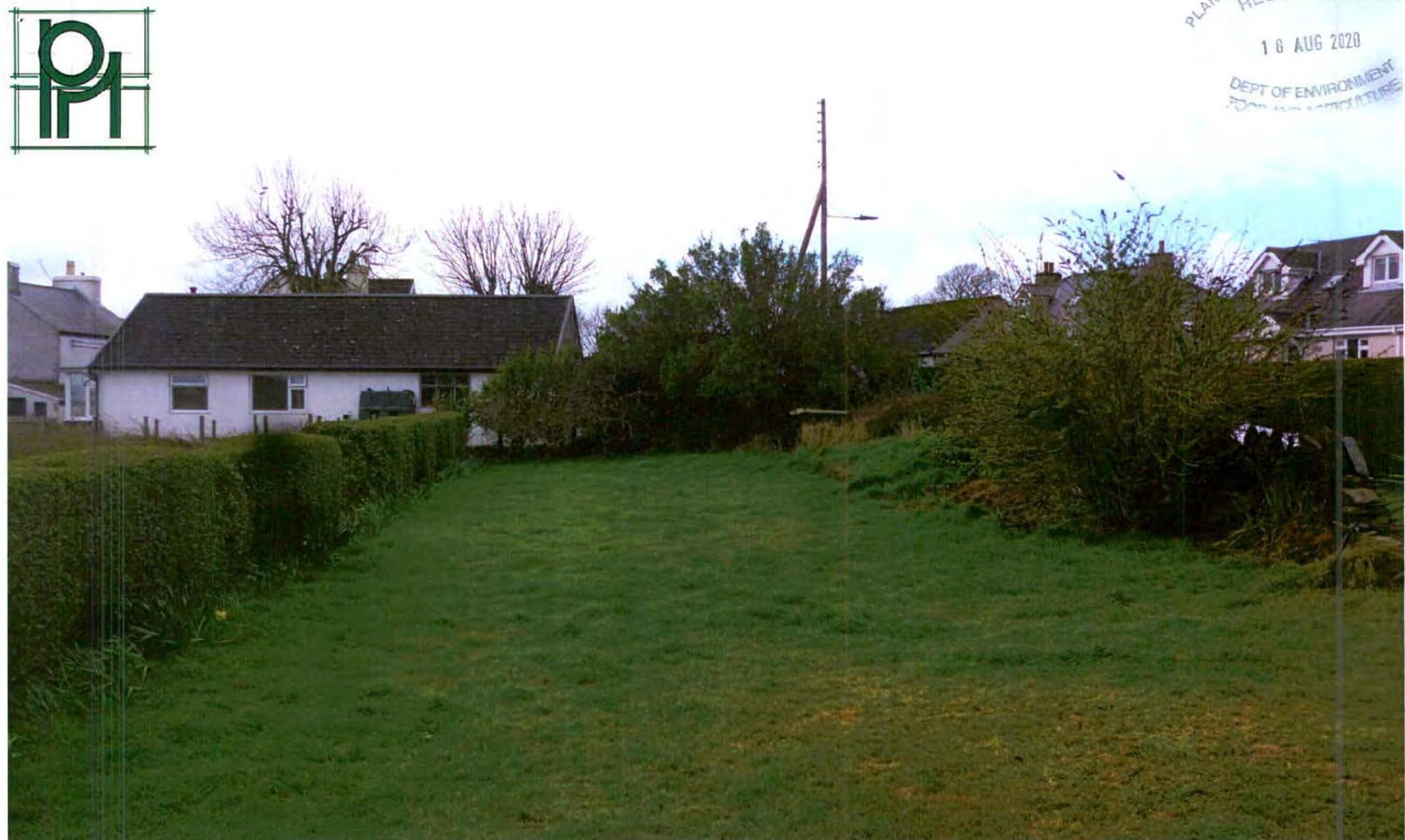 A photograph showing a grassy rear garden area bordered by hedges, with a white single-story bungalow visible in the background.