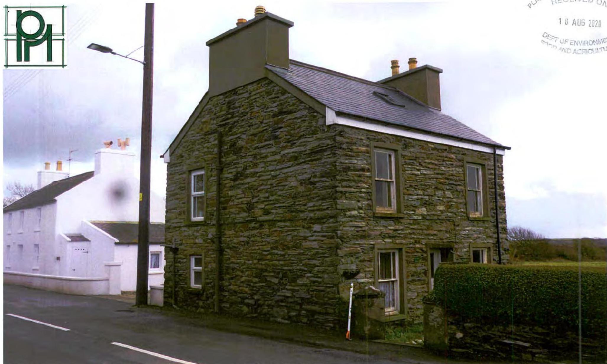 A street-level photograph showing the existing two-storey stone dwelling with a slate roof and chimneys, situated next to a white building.