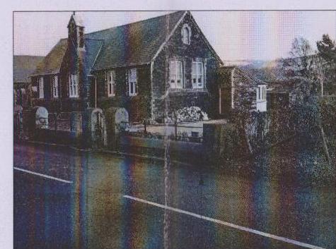A grainy photograph showing the exterior of a large detached house with a pitched roof situated alongside a road.
