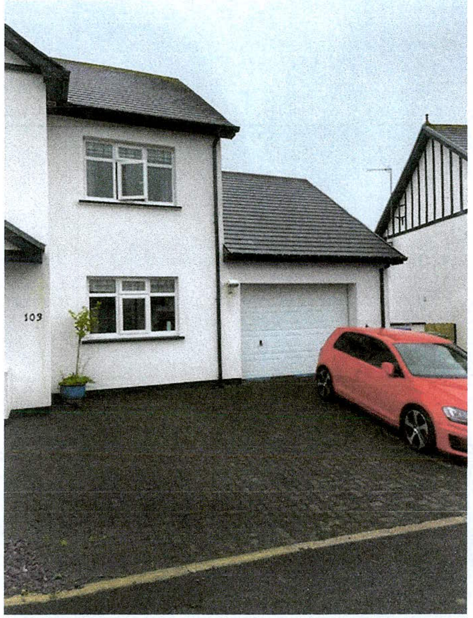 A photograph showing the front exterior of a white two-story detached house with an attached garage and a red car parked in the driveway.