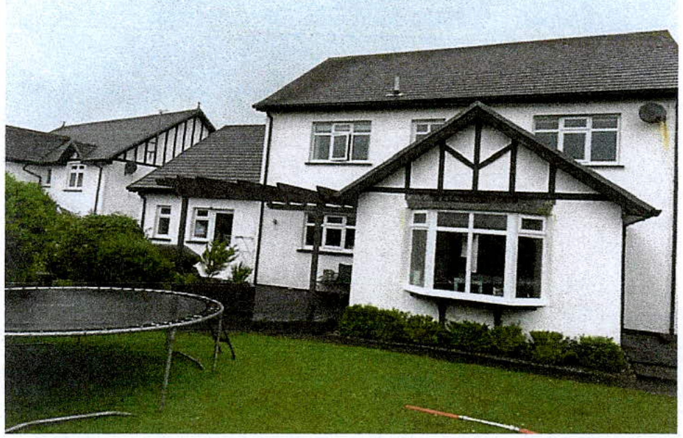 A photograph showing the rear exterior of a white two-story detached house with a bay window and a trampoline in the garden.