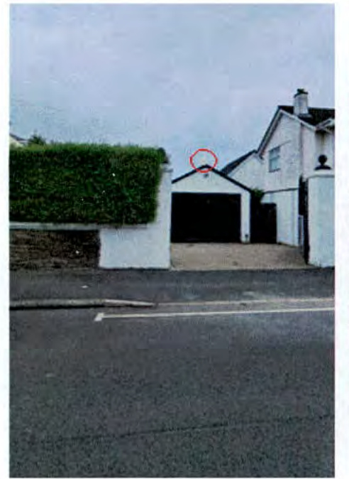 A photograph of a residential property showing a white garage and boundary wall, with a red circle marking the roof ridge.