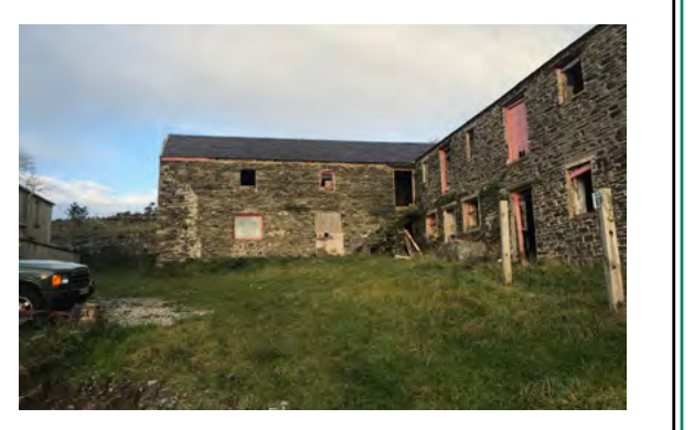 A photograph showing a dilapidated stone agricultural building, likely a barn, with open window frames and a grassy foreground.
