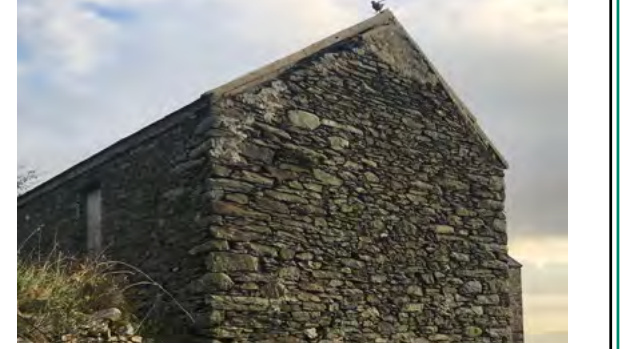 A photograph showing the gable end of a traditional stone building, likely a barn or outbuilding, with a bird perched on the roof ridge against a cloudy sky.