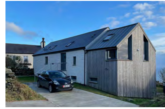 A photograph of a modern rural dwelling featuring mixed white render and vertical timber cladding, with a car parked on the driveway.