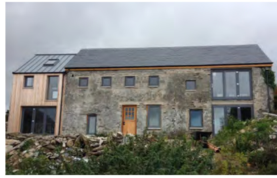 A photograph showing a stone building with a modern timber-clad extension featuring large windows and a slate roof.