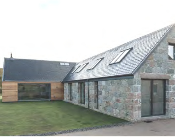 A photograph showing the exterior of a modern residential property featuring a stone facade and wooden cladding with a slate roof and skylights.