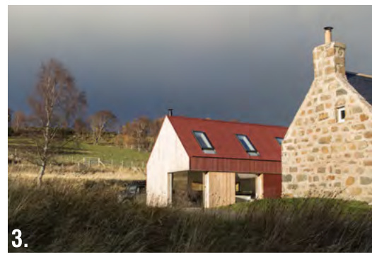 A photograph showing a modern single-story extension with a red roof attached to an existing stone building in a rural landscape.