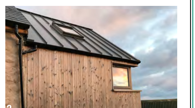 A photograph showing the upper section of a building with vertical timber cladding, a dark pitched roof, and a skylight window.