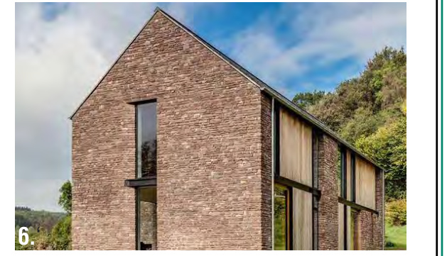A photograph or architectural rendering of a modern detached house featuring stone cladding, large windows, and a pitched roof set against a rural backdrop.