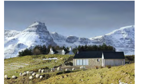 A photograph showing a stone building, likely a converted barn or new dwelling, situated on a grassy hillside with sheep grazing in the foreground and snow-capped mountains in the background.