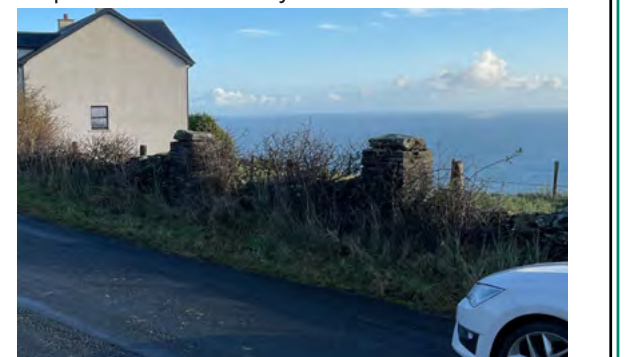 A photograph showing a white detached house with a stone boundary wall overlooking the sea, with a car parked on the road in the foreground.