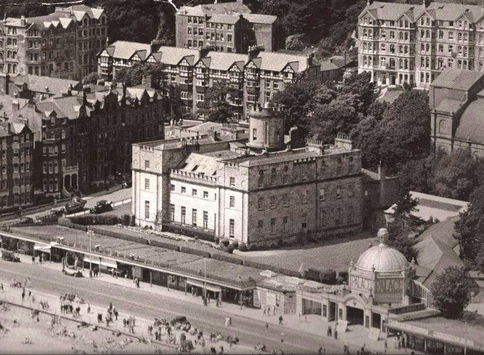 A black and white aerial photograph showing a large historic building complex near a beach, featuring a domed structure labeled 'PALACE' in the foreground.
