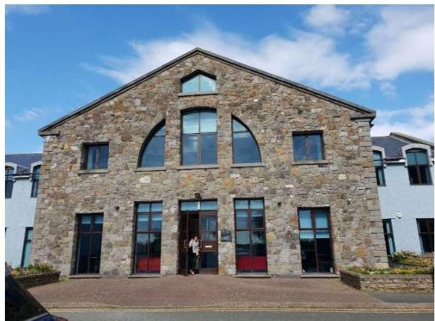 A photograph showing the front elevation of a large, two-story stone building with arched windows and a paved forecourt.