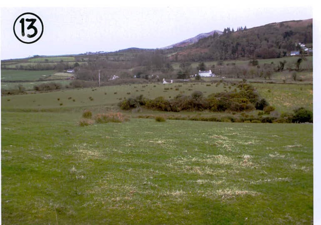 A photograph showing a rural landscape with green fields and scattered houses in the distance, likely depicting the site context for the planning application.