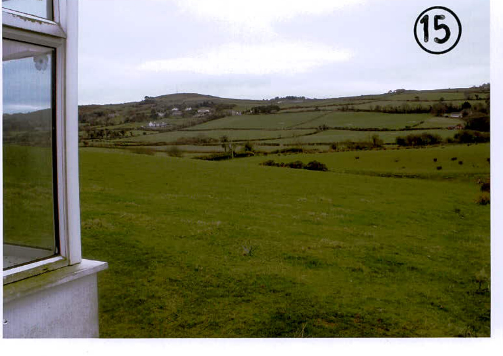 A photograph taken from a window looking out over green agricultural fields and rolling hills in a rural setting.
