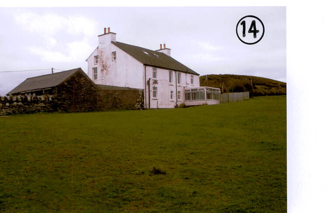 A photograph showing a white two-story detached house with a conservatory and an adjacent stone outbuilding situated in a large grassy field.