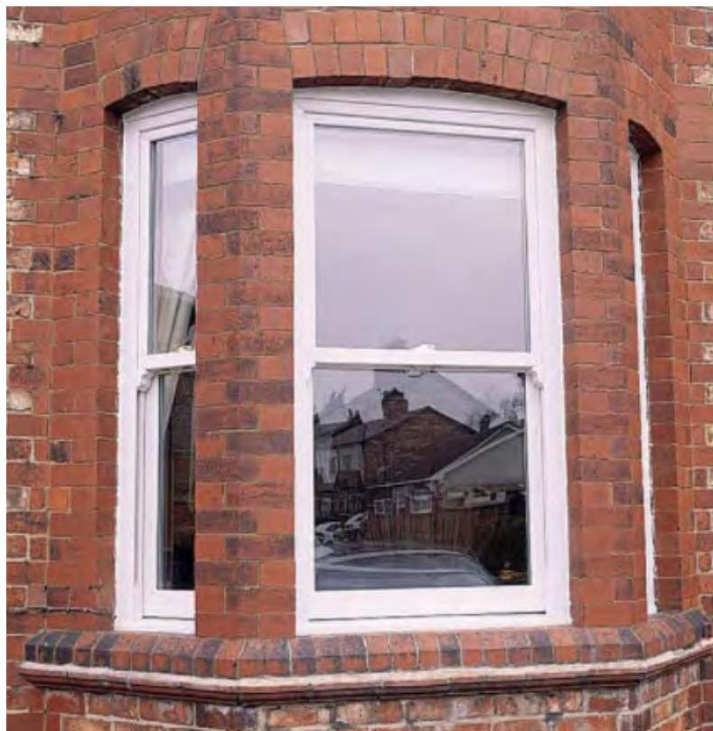 A close-up photograph of a red brick bay window featuring white uPVC sliding sash windows.