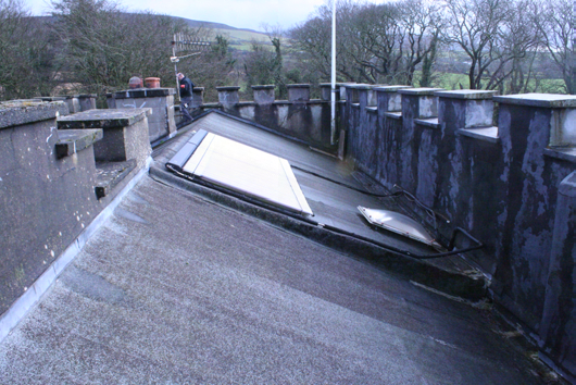 A photograph showing a close-up view of a roof section with stone parapet walls, featuring white boards lying on the surface, likely during the refurbishment works described in the application.