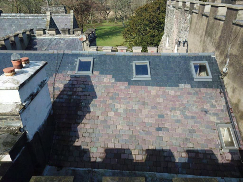 A high-angle photograph showing a slate roof with skylights and chimneys, likely part of a refurbishment project.