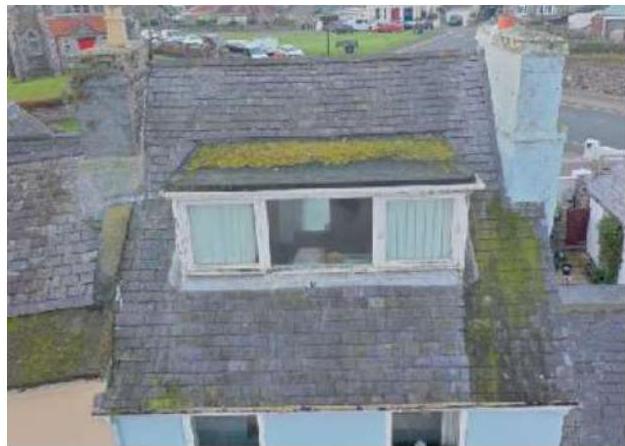 A high-angle photograph showing a slate roof with a dormer window extension and a chimney stack.