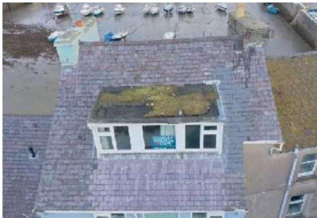 Aerial photograph of a slate roof featuring a dormer window, with a harbor and boats visible in the background.