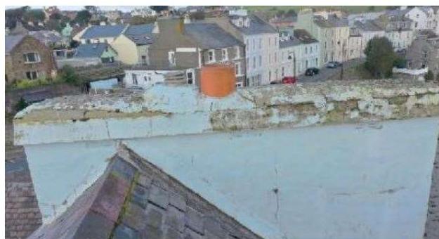 A high-angle photograph taken from a roof showing a weathered white wall and chimney pot, overlooking a street of terraced houses.