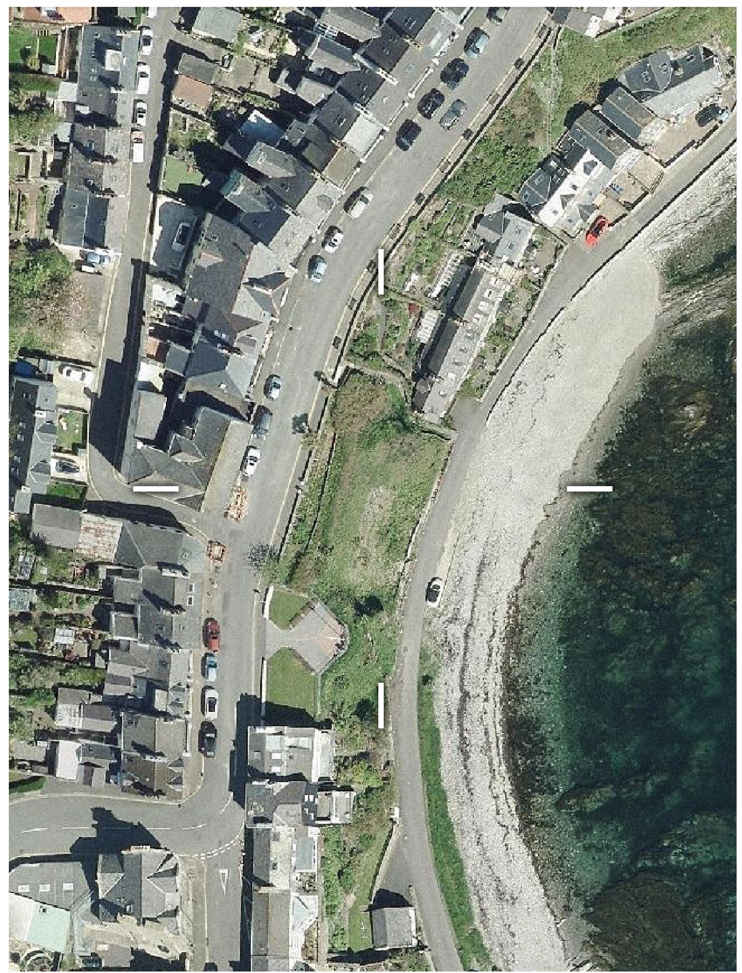 Aerial site location map showing a coastal road, residential properties, and a beach with white boundary markers indicating the plot.