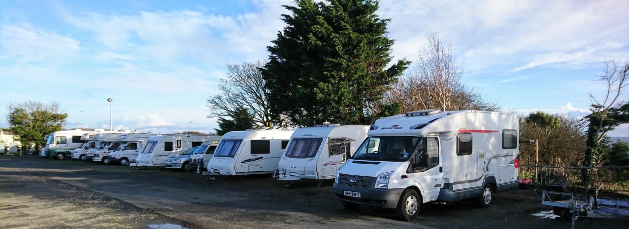 A photograph showing a row of white motorhomes and caravans parked on a gravel surface.