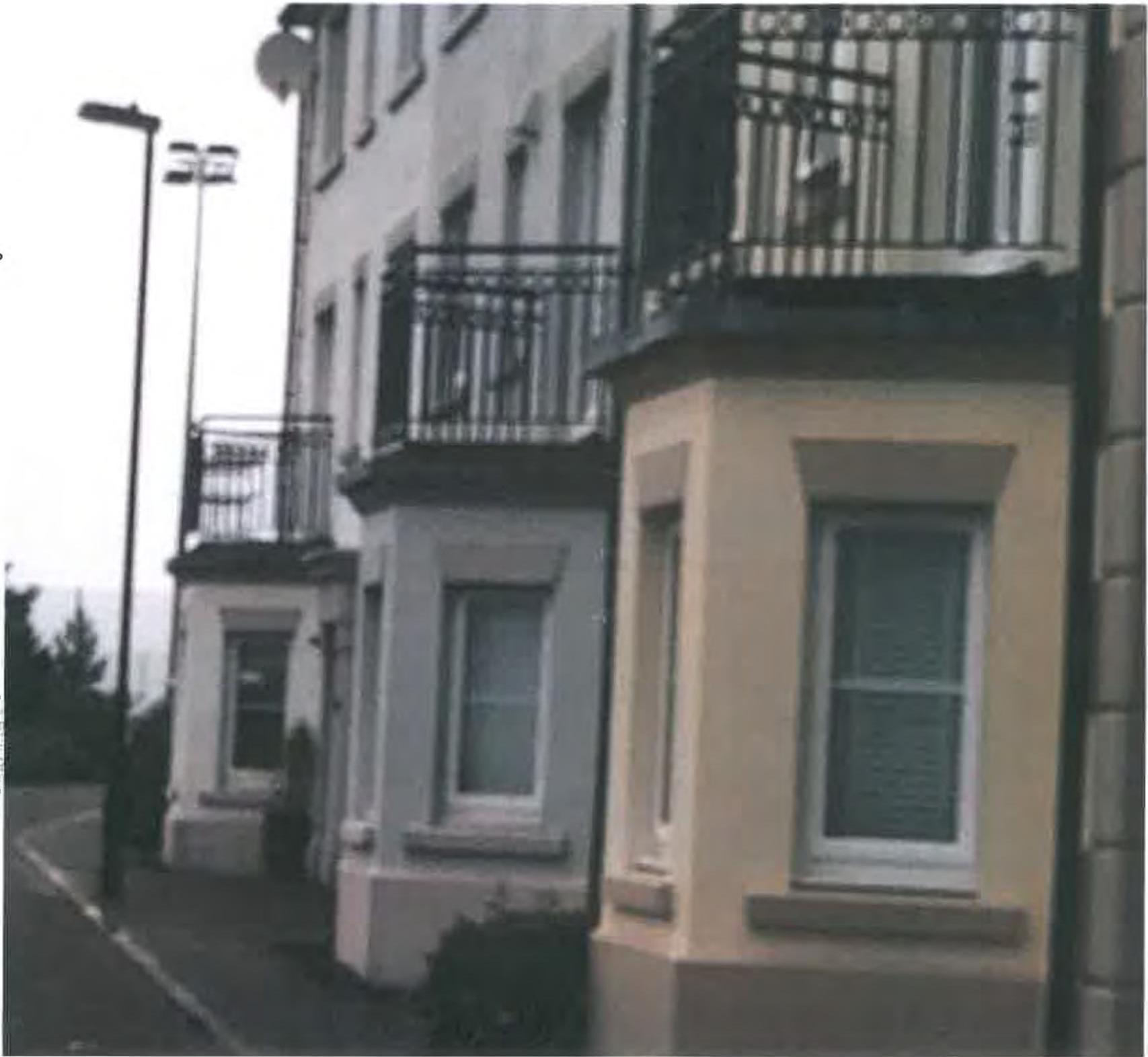 A grainy black and white photograph showing the exterior facade of a row of terraced houses with bay windows and balconies.