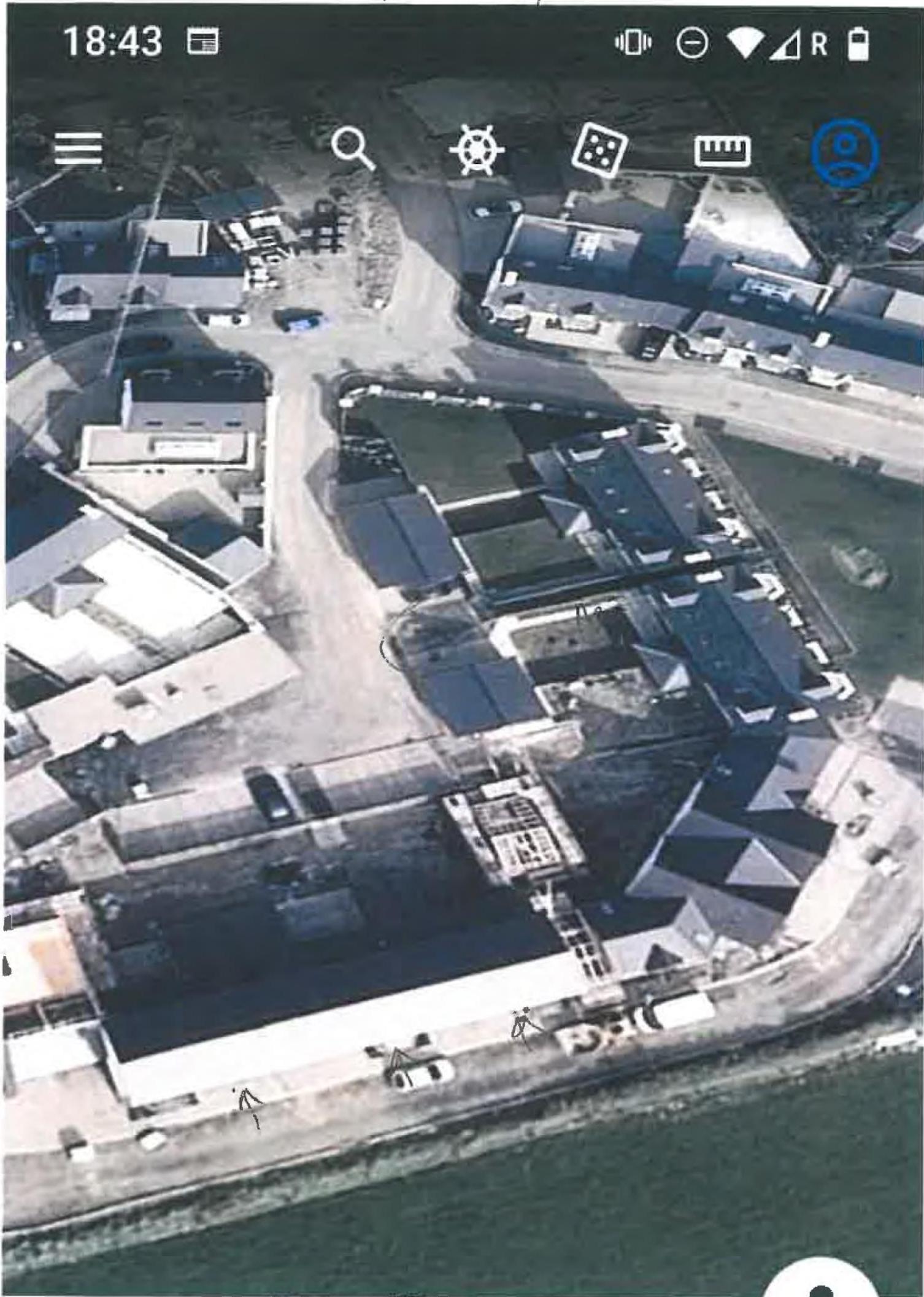 A screenshot from a mapping application showing an aerial view of a coastal site with surrounding buildings and the sea.