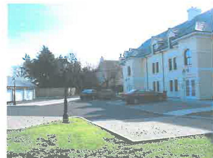 A low-quality, overexposed photograph showing a street scene with a large building on the right, parked cars, and a grassy foreground area.