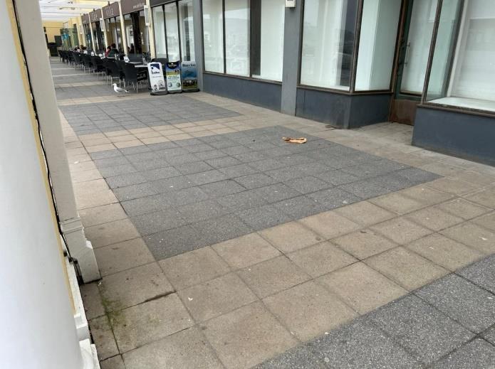 A photograph showing the paved pavement and storefronts of a commercial unit with outdoor seating.