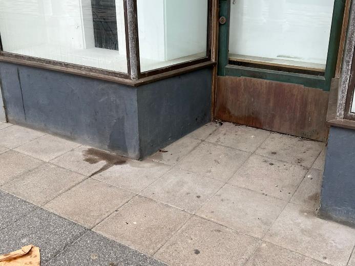 A photograph showing the ground floor exterior of a commercial property, featuring large display windows and a door with a wooden panel.