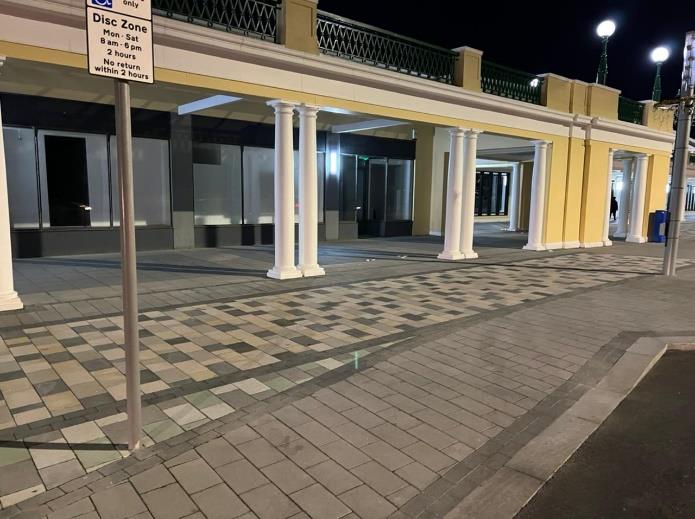 Night-time photograph of a commercial building exterior featuring a colonnade with white pillars and large glass windows.