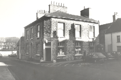 A black and white photograph showing the exterior of a two-story stone building on a street corner, likely the subject of the planning application.