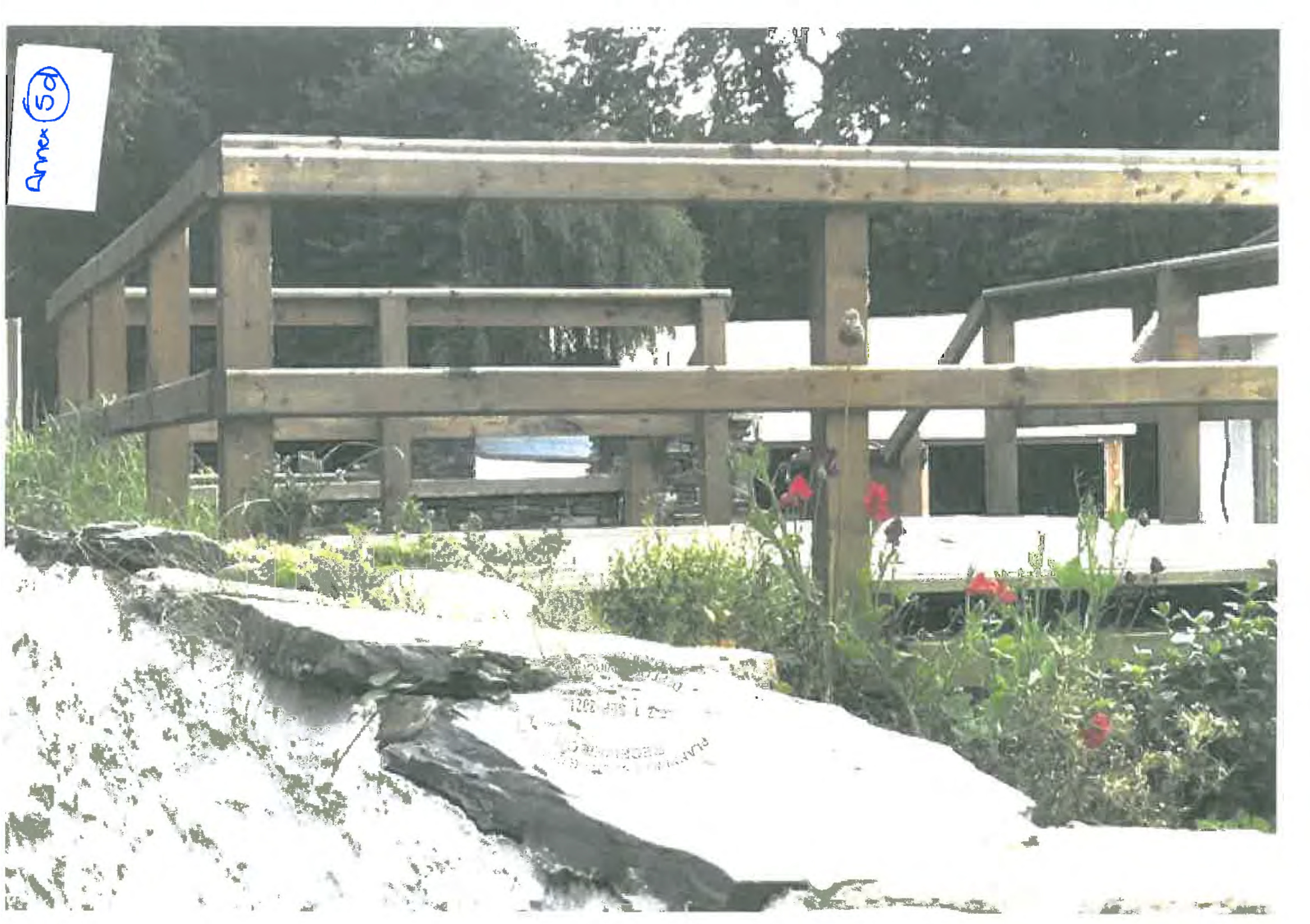 A photograph showing the wooden frame of a raised deck under construction in a garden setting with a stone wall in the foreground.
