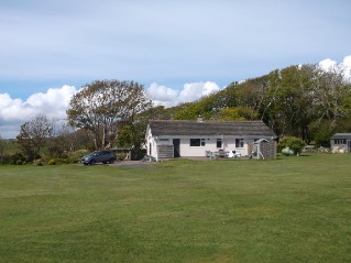 A photograph showing a white detached bungalow situated in a rural setting with a large grassy foreground and trees in the background.