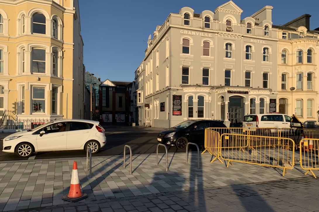 A street-level photograph showing the exterior of the Granville Hotel and an adjacent yellow building in Douglas, with parked cars and street furniture in the foreground.