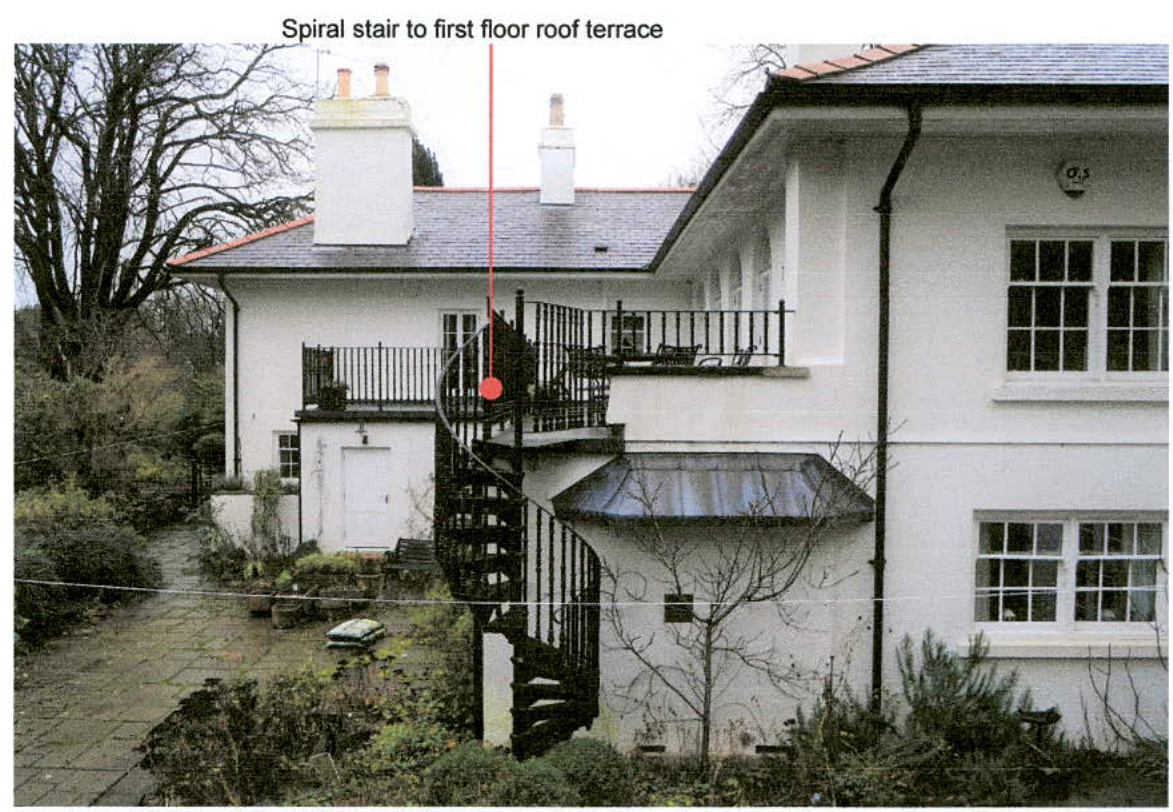 An annotated photograph showing the exterior of a white detached house with a black spiral staircase leading to a first-floor terrace.